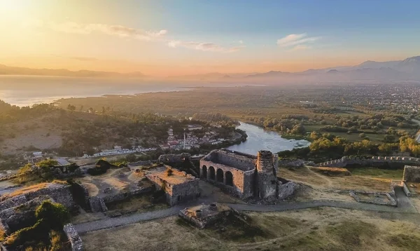 Arnavutluk 'taki Rozafa Kalesi' nin havadan insansız hava aracı görüntüsü yıkılıyor. Ortaçağ kalesi ve günbatımında St Stephens Kilisesi 'nin kalıntıları, Buna Nehri ve Shkoder Gölü' ne bakan arka planda dağlar..