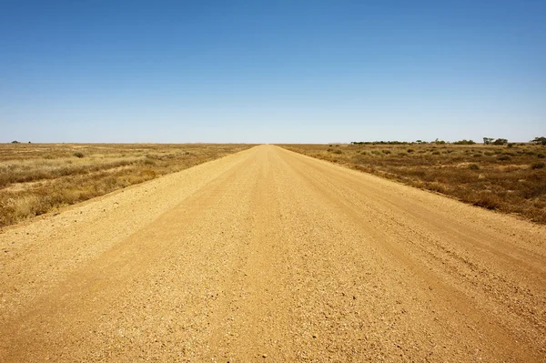 A long, straight dirt road in the desert. — Stock Photo, Image