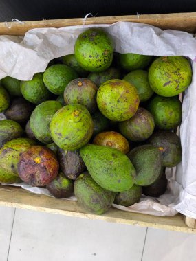 Olgun ve olgunlaşmış avokado yığını beyaz kağıtlarla kaplanmış kırsal bir ahşap sandığa doldurulmuş bir sürü yeşil ve koyu renkli meyve pazara hazır.