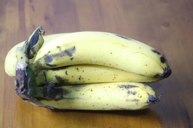 Sıcak ahşap zemin üzerinde duran, karakteristik şeker lekeleri olan olgun sarı muzlar.