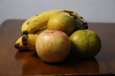 Elma, muz ve portakallar da dahil olmak üzere olgun meyvelerin renkli bir karışımı cilalanmış ahşap bir yüzeyde oturuyor.