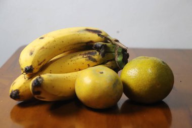 Kahverengi benekli ve iki portakallı olgun sarı muzlar parlak ahşap bir yüzey üzerinde dinleniyor.