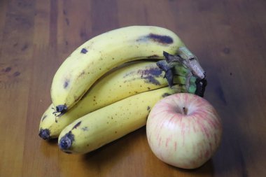 Kahverengi şeker lekeli olgun muzlar ve tahtadan bir yüzey üzerinde taze bir elma dinleniyor.