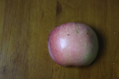 Derisinin üzerinde küçük bir karınca sürünen taze pembe bir elma manzarası, sıcak ahşap bir arka plan üzerine kurulmuş.