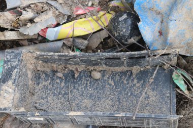 Çamurla kaplı plastik sandık, muşamba ve diğer ıvır zıvırların çevresel kirliliği vurguluyor.