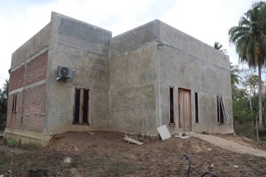 İnşaat halindeki bir evin dış görünüşü, boyanmamış beton duvarlar ve doğal bir şekilde korunmasız tuğlalar.