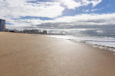Güzel, güzel, geniş kumlu bir sahil, Atlantik kıyısında ıssız. Gökyüzü manzarası ve Rota 'ya doğru, Playa de la Costilla' da güneş ışığı, Costa de la Luz, Cdiz, Endülüs, İspanya.