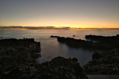 Şafak vakti La Palma 'nın engebeli lav kıyısındaki taş bir binanın siluetli kalıntıları. Yumuşak bulutlar ve Atlantik Okyanusu üzerinde pembemsi bir ufuk ile uzun pozlama.