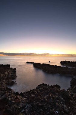 Şafak vakti La Palma 'nın engebeli lav kıyısındaki taş bir binanın siluetli kalıntıları. Yumuşak bulutlar ve Atlantik Okyanusu üzerinde pembemsi bir ufuk ile uzun pozlama.