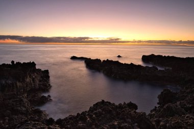 Şafak vakti La Palma 'nın engebeli lav kıyısındaki taş bir binanın siluetli kalıntıları. Yumuşak bulutlar ve Atlantik Okyanusu üzerinde pembemsi bir ufuk ile uzun pozlama.