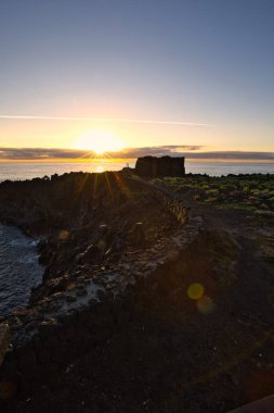 Şafak vakti La Palma 'nın engebeli lav kıyısındaki taş bir binanın siluetli kalıntıları. Yumuşak bulutlar ve Atlantik Okyanusu üzerinde pembemsi bir ufuk ile uzun pozlama.