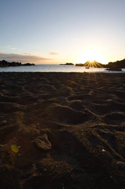 La Palma 'daki Los Cancajos' un kara kumsalında gün doğumu. Volkanik kayaların arkasında güneş patlaması var..
