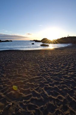La Palma 'daki Los Cancajos' un kara kumsalında gün doğumu. Volkanik kayaların arkasında güneş patlaması var..