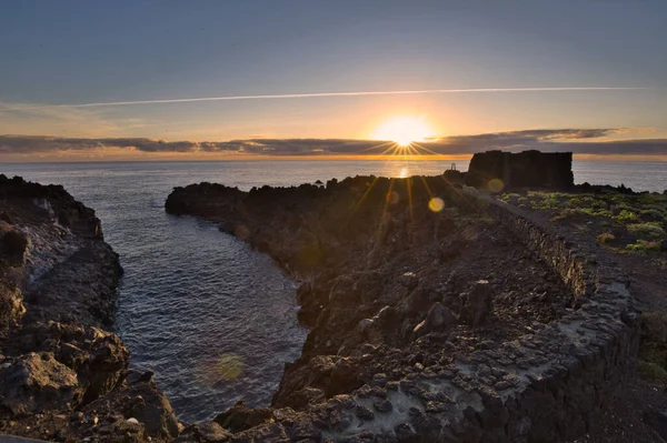 Şafak vakti La Palma 'nın engebeli lav kıyısındaki taş bir binanın siluetli kalıntıları. Yumuşak bulutlar ve Atlantik Okyanusu üzerinde pembemsi bir ufuk ile uzun pozlama.