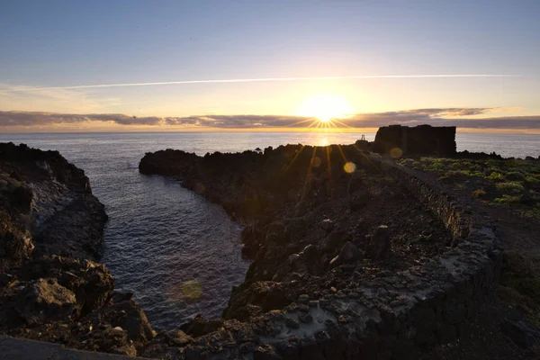 Şafak vakti La Palma 'nın engebeli lav kıyısındaki taş bir binanın siluetli kalıntıları. Yumuşak bulutlar ve Atlantik Okyanusu üzerinde pembemsi bir ufuk ile uzun pozlama.