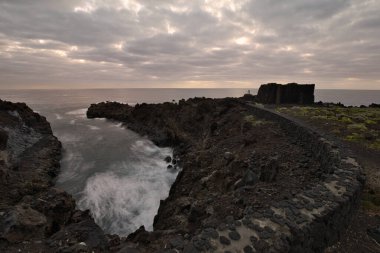 Los Cancajos, La Palma 'nın dramatik volkanik kıyı şeridi. Kara bazalt kaya oluşumları kasvetli bir gökyüzünün altında Atlantik Okyanusu ile buluşur. Kanarya Adalarında Manzaralı Seyahat