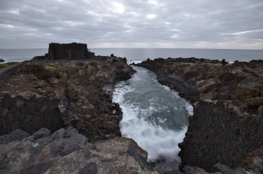 Los Cancajos, La Palma 'nın dramatik volkanik kıyı şeridi. Kara bazalt kaya oluşumları kasvetli bir gökyüzünün altında Atlantik Okyanusu ile buluşur. Kanarya Adalarında Manzaralı Seyahat