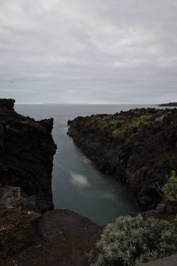 Los Cancajos, La Palma 'nın dramatik volkanik kıyı şeridi. Kara bazalt kaya oluşumları kasvetli bir gökyüzünün altında Atlantik Okyanusu ile buluşur. Kanarya Adalarında Manzaralı Seyahat
