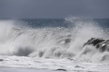 Büyük bir Atlantik dalgası Tazacorte sahiline çarpıyor. Beyaz köpük ve spreyle kırılan turkuaz suyun yakın çekimi denizin evcilleştirilmemiş gücünü gösteriyor. La Palma, Kanarya Adaları, İspanya