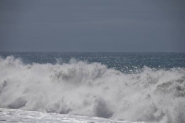 Büyük bir Atlantik dalgası Tazacorte sahiline çarpıyor. Beyaz köpük ve spreyle kırılan turkuaz suyun yakın çekimi denizin evcilleştirilmemiş gücünü gösteriyor. La Palma, Kanarya Adaları, İspanya