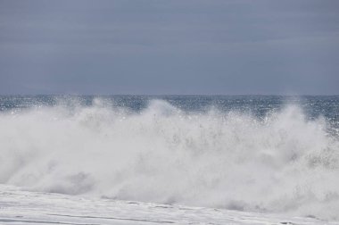 Büyük bir Atlantik dalgası Tazacorte sahiline çarpıyor. Beyaz köpük ve spreyle kırılan turkuaz suyun yakın çekimi denizin evcilleştirilmemiş gücünü gösteriyor. La Palma, Kanarya Adaları, İspanya