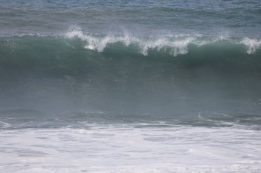 Büyük bir Atlantik dalgası Tazacorte sahiline çarpıyor. Beyaz köpük ve spreyle kırılan turkuaz suyun yakın çekimi denizin evcilleştirilmemiş gücünü gösteriyor. La Palma, Kanarya Adaları, İspanya