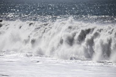 Büyük bir Atlantik dalgası Tazacorte sahiline çarpıyor. Beyaz köpük ve spreyle kırılan turkuaz suyun yakın çekimi denizin evcilleştirilmemiş gücünü gösteriyor. La Palma, Kanarya Adaları, İspanya