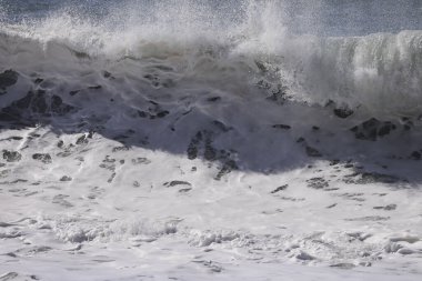 Büyük bir Atlantik dalgası Tazacorte sahiline çarpıyor. Beyaz köpük ve spreyle kırılan turkuaz suyun yakın çekimi denizin evcilleştirilmemiş gücünü gösteriyor. La Palma, Kanarya Adaları, İspanya