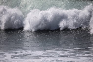 Büyük bir Atlantik dalgası Tazacorte sahiline çarpıyor. Beyaz köpük ve spreyle kırılan turkuaz suyun yakın çekimi denizin evcilleştirilmemiş gücünü gösteriyor. La Palma, Kanarya Adaları, İspanya