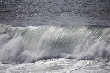 Büyük bir Atlantik dalgası Tazacorte sahiline çarpıyor. Beyaz köpük ve spreyle kırılan turkuaz suyun yakın çekimi denizin evcilleştirilmemiş gücünü gösteriyor. La Palma, Kanarya Adaları, İspanya