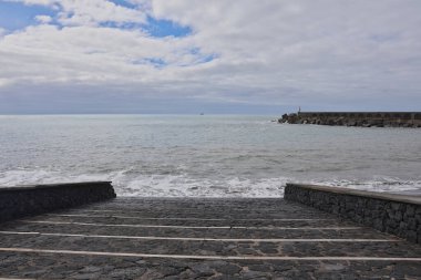 Şiddetli Atlantik dalgaları taş merdivenlere ve Tazacorte limanının dalgalanan sularına çarpıyor. La Palma kıyısındaki karanlık volkanik kayaların üzerine yüksek su püskürtüsü ve köpük..