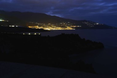 Santa Cruz de La Palma, Kanarya Adaları 'nda uzun süre volkanik kayalık sahile maruz kaldı. Arka planda şehir ışıkları ve Atlantik Okyanusu üzerinde dramatik bulutlu gökyüzü vardı.