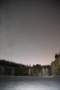 İsveç 'teki kayalık bir taş ocağında, sarp kayalıklarda donmuş buz şelaleleri ve kışın milyonlarca yıldızın altında yoğun bir çam ormanı bulunan Samanyolu' nun nefes kesici gece manzarası.