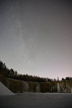 İsveç 'teki kayalık bir taş ocağında, sarp kayalıklarda donmuş buz şelaleleri ve kışın milyonlarca yıldızın altında yoğun bir çam ormanı bulunan Samanyolu' nun nefes kesici gece manzarası.