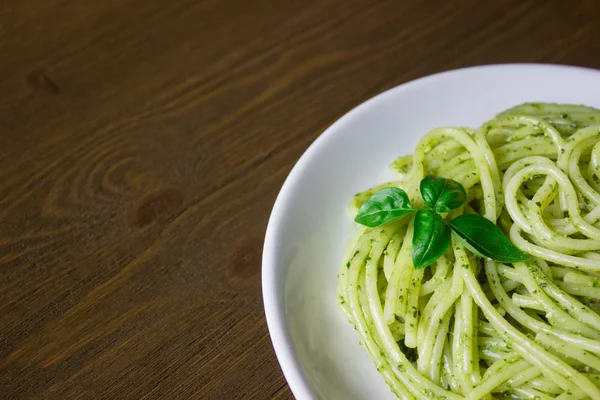 Pasta con salsa de pesto y hojas de albahaca sobre plato blanco, fondo de madera, vista superior — Foto de Stock