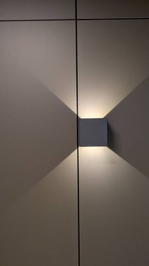 Yanan duvar lambası geometrik gölgeleri panelli yüzey boyunca döküyor, sıcak ortam parlaklığı ve çıtır çıtır olan modern iç tasarım sahnesi.