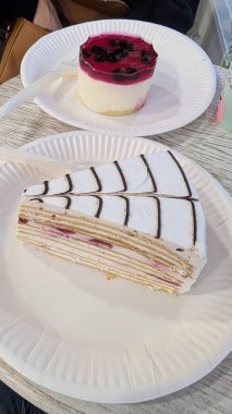 Tabakta katmanlı krep dilimi, arka planda ahududu kreması, çikolata ağ kreması, ince krep katmanları görünür, kağıt tabak.