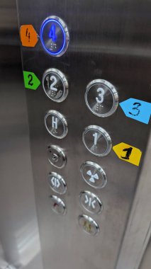 Kapalı asansör düğmesi paneli paslanmaz çelik yüzey üzerinde numaralandırılmış kontrolleri ve renkli etiketleri gösterir, dokunulabilir yuvarlak tuşlar