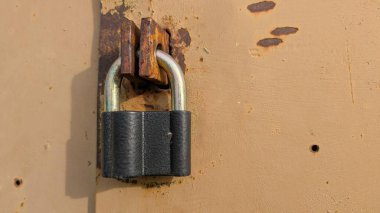 Metal kapıdaki asma kilit paslanmış hasp kırıntısı bej boya, aşındırıcı desenli sıcak güneş ışığı.