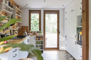 Kır evindeki pencereli, rahat ahşap mutfağın içi. Mutfak lavabosu ve mutfak dolapları olan klasik mutfak eşyaları ve kırsal dekorlar. İçerisi aydınlık.