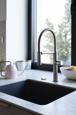 Pencerenin yanında gümüş musluk ve granit tezgahı olan modern mutfak lavabosu. Mutfağın içi detaylarla dolu. Kapatın. Dikey.