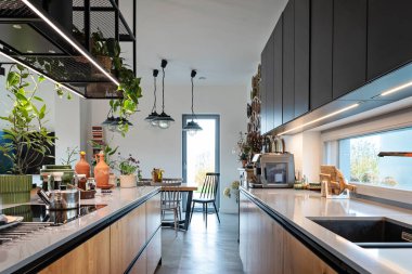 Mutfak adasının üzerinde rafları olan siyah lüks mobilyaları ve lambaları olan modern bir mutfak. Mutfak lavabosunun yanındaki pencere ve ışık. Tasarım tarzına sahip akıllı ev.