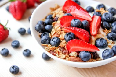 Sağlıklı kahvaltı kavramı. Granola yaban mersini ve beyaz kase çilek ile.