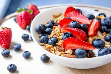 Sağlıklı kahvaltı kavramı. Granola yaban mersini ve beyaz kase çilek ile.
