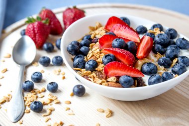 Sağlıklı kahvaltı kavramı. Granola yaban mersini ve beyaz kase çilek ile.