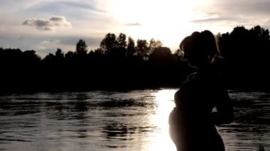 Hamile kadının karnı üzerinde arka plan günbatımı nehirde pats