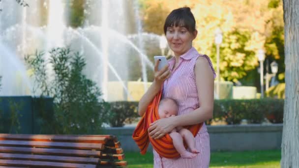 Giovane donna con bambino addormentato in fionda sorprende felicemente sul messaggio telefonico — Video Stock