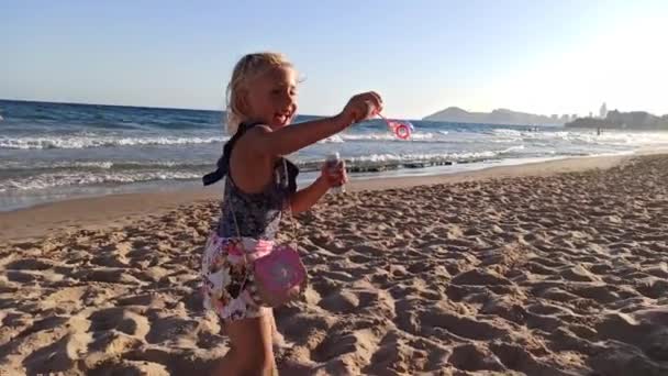 Criança sopra bolhas de sabão na praia — Vídeo de Stock