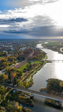 Hava görüntüsü Malbork Kalesi 'ni gösteriyor. Polonya' nın Malbork şehrinde, kırmızı tuğla duvarlar, taretler, köprüler ve Nogat Nehri 'nin kenarındaki kiremitli çatılar öğleden sonra ışığı ve bulutlarla kaplı..