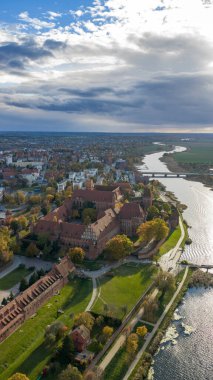 Yüksek irtifa havası kuzey Polonya 'da Malbork Kalesi ve Nogat Nehri' ni gösteriyor. Kırmızı tuğla duvarlar, kuleler, çatılar, çimenler, yollar, sonbahar ağaçları, köprüler ve gümüş renkli gölgeler.